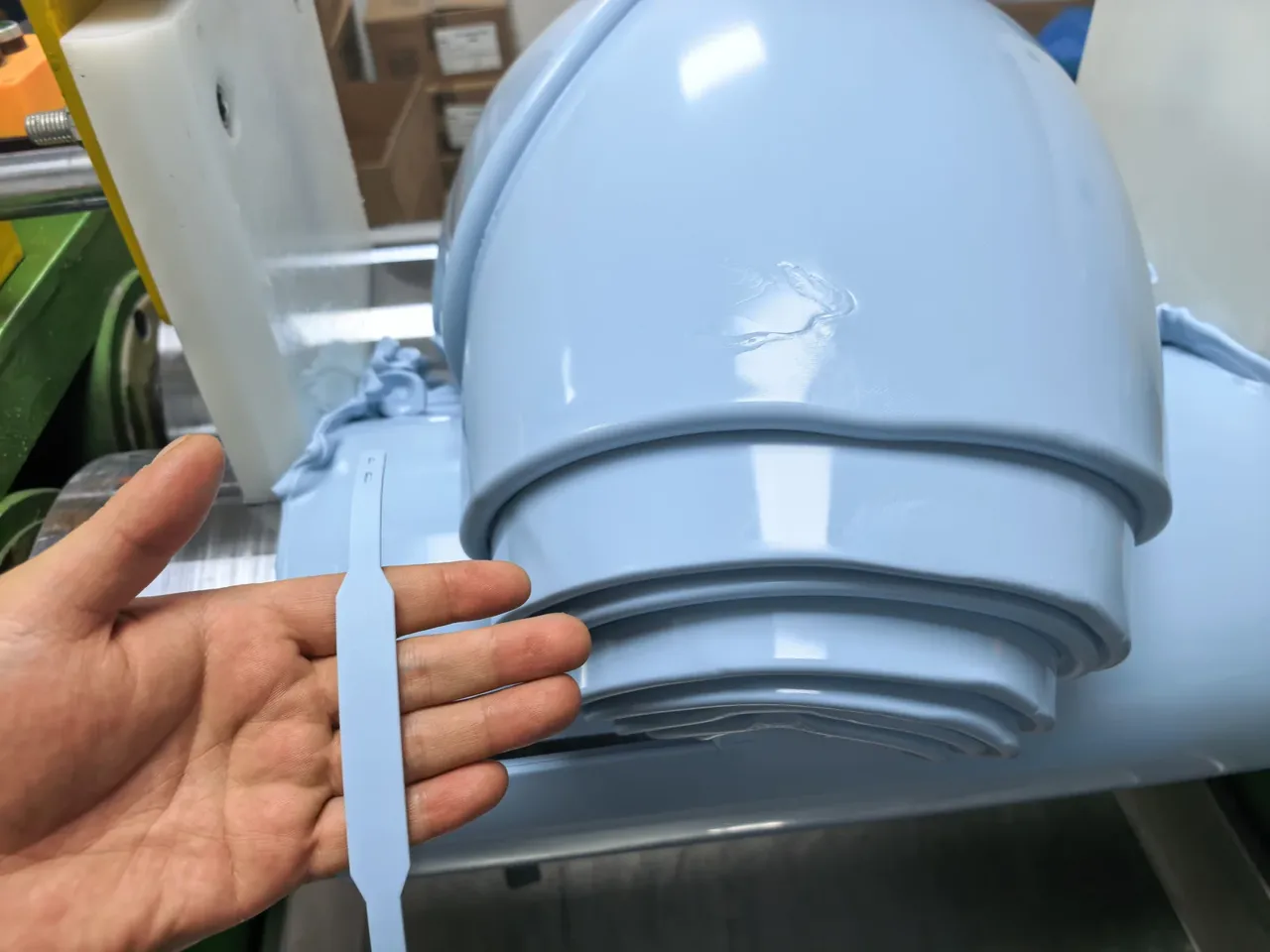 A hand holding a plain flexible strap near the mixing equipment