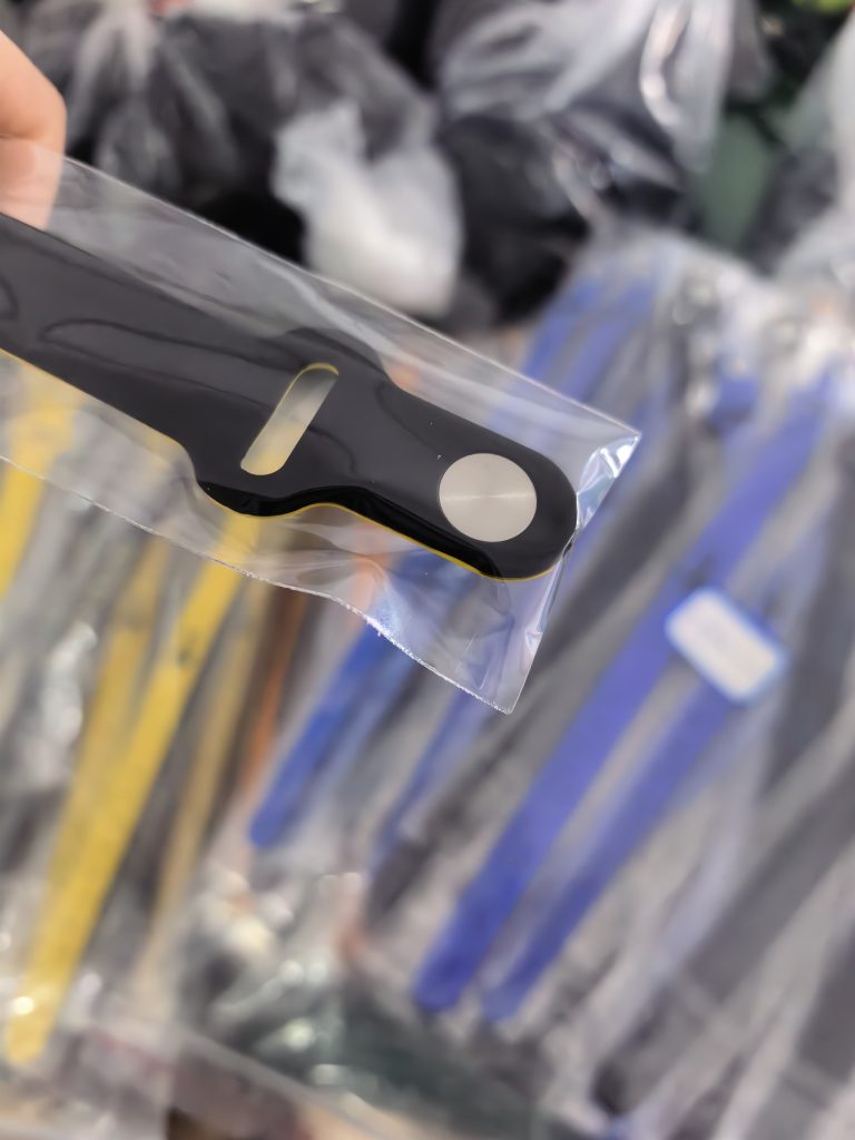Packaged black and yellow wristband end with a metal fastener back and tail slot visible through clear plastic